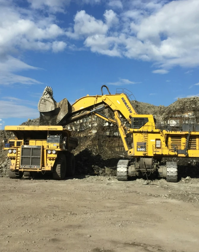 Buldożer marki Komatsu przesuwający gruz w kamieniołomie. Ciężki sprzęt pracuje przy wydobyciu skał i ziemi, geologiczne zjawisko w akcji.